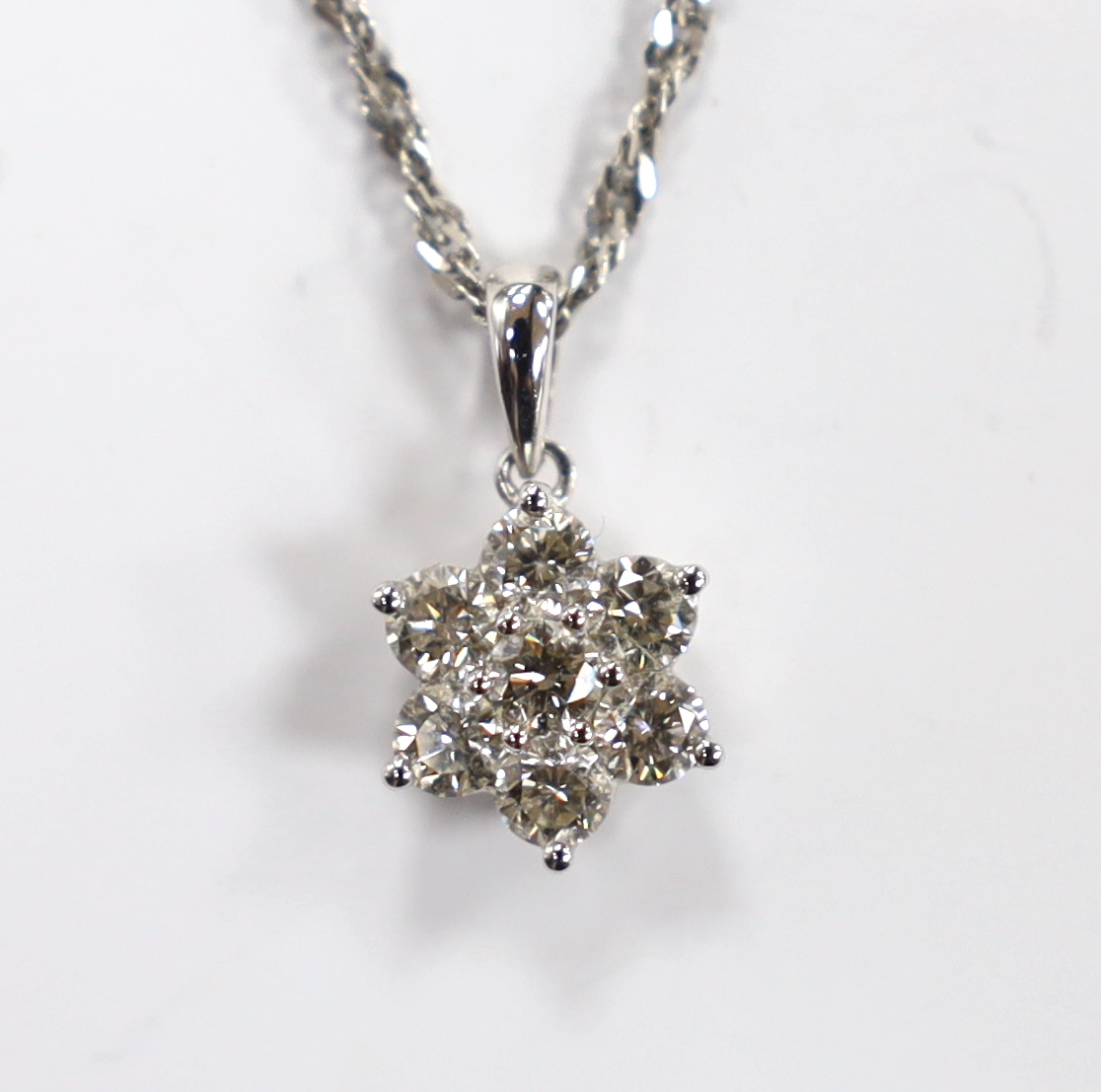 A modern 18k white metal and seven stone diamond cluster set flower head pendant, overall 15mm, on a 9ct white gold chain, 45cm, gross weight 3.2 grams.